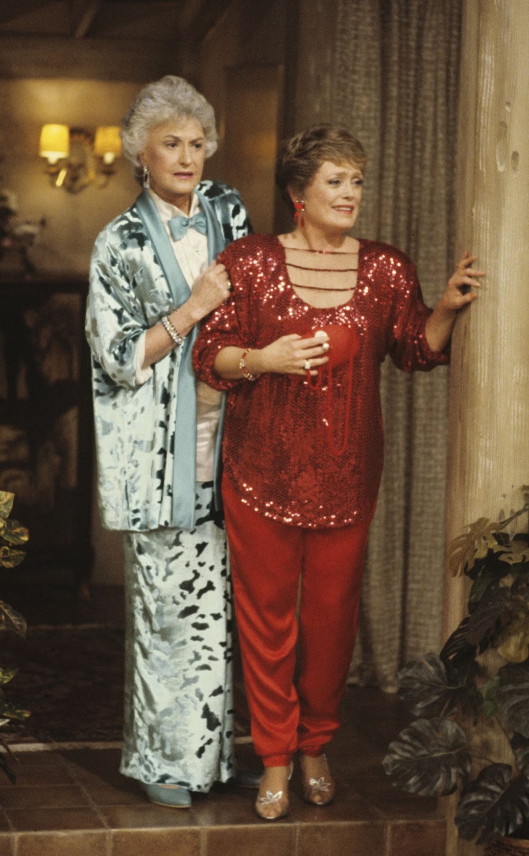 Dorothy wearing a floor length crushed velvet mint green skirt with matching jacket and bow tie, Blanche in a shiny red velvet trouser suit with strands split across the chest
